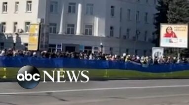 Protesters carry large Ukrainian flag past armored vehicles in Kherson